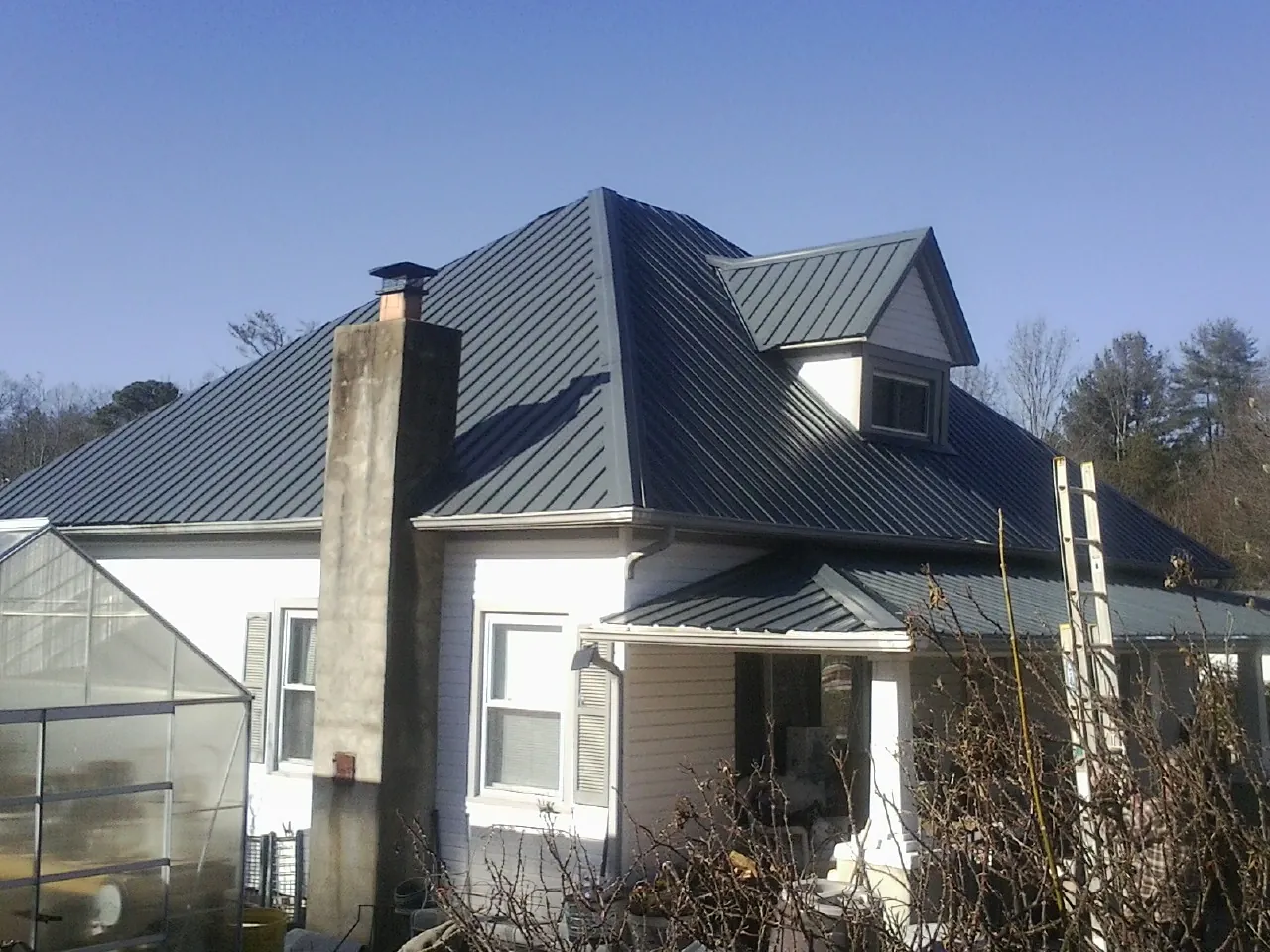 Dark blue standing seam metal roof on a white farmhouse with dormer — Slate & Tile Roof Repair by Roofing Brothers in Schuyler