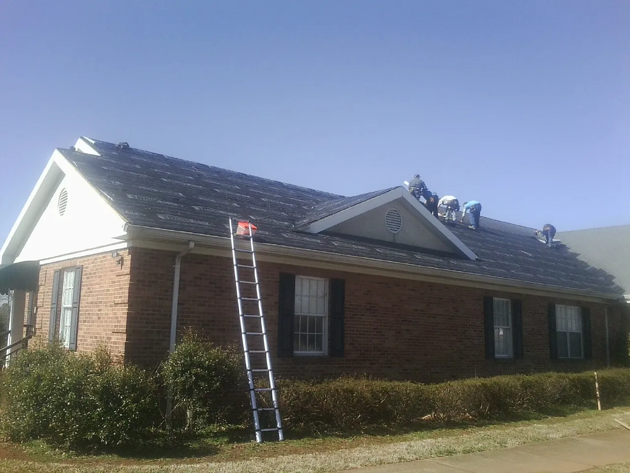 Crew tearing shingles off a brick ranch roof with a ladder set — Emergency Roof Repair work by our crew in Schuyler