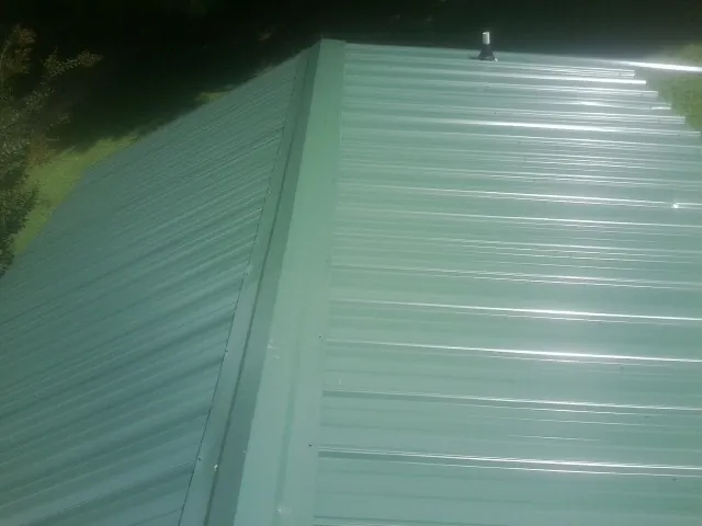 New green metal panels meeting at the ridge of a roof — Flat Roof Repair work by our crew in Schuyler