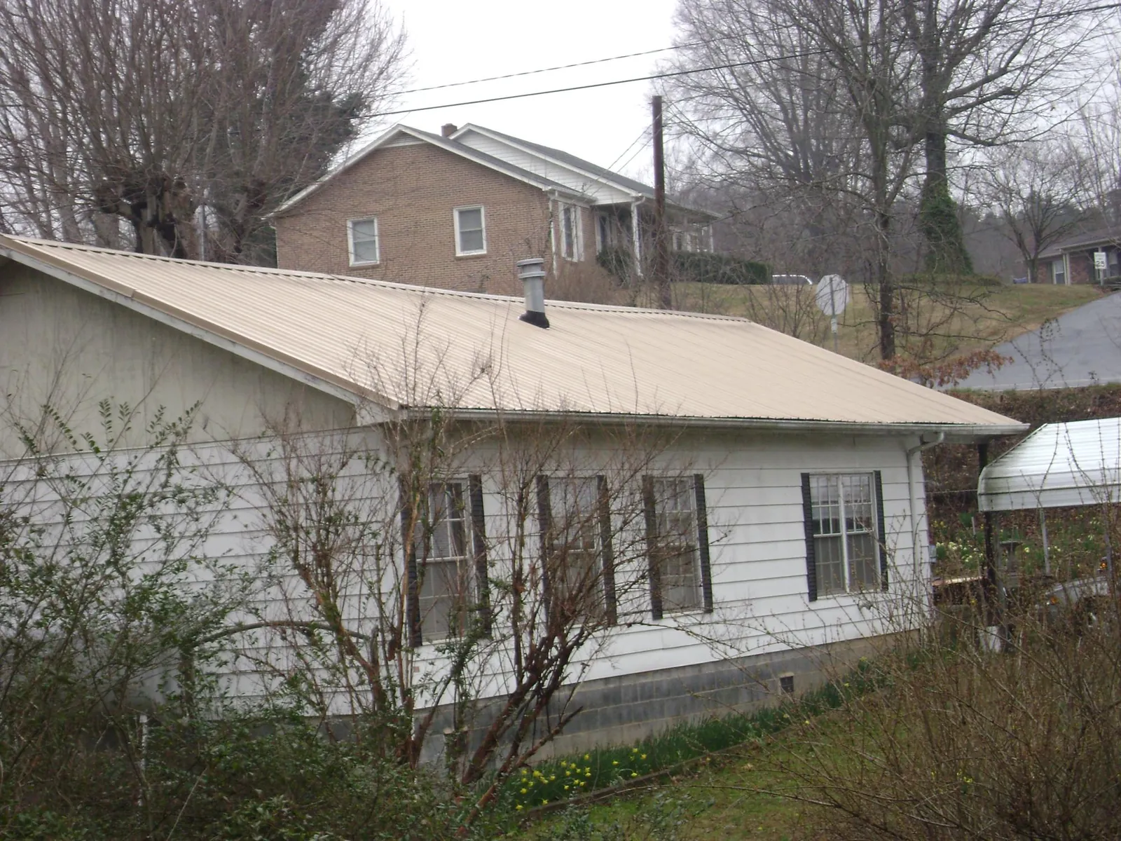 Tan metal roof on a white sided house set into a hillside — Commercial Roofing by Roofing Brothers in Schuyler